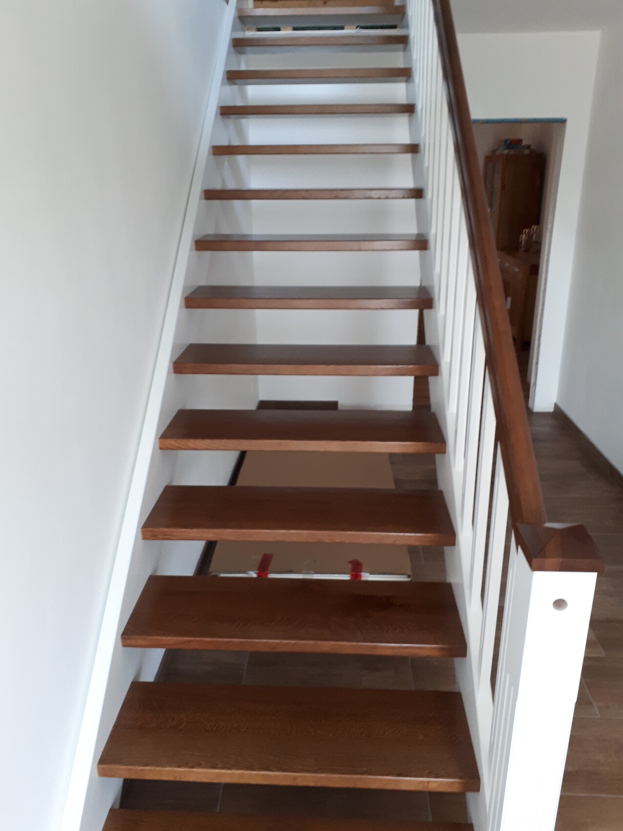 Innenraum-Treppe aus dunklem Holz mit offenen Stufen, weißem Geländer und seitlichem Handlauf.
