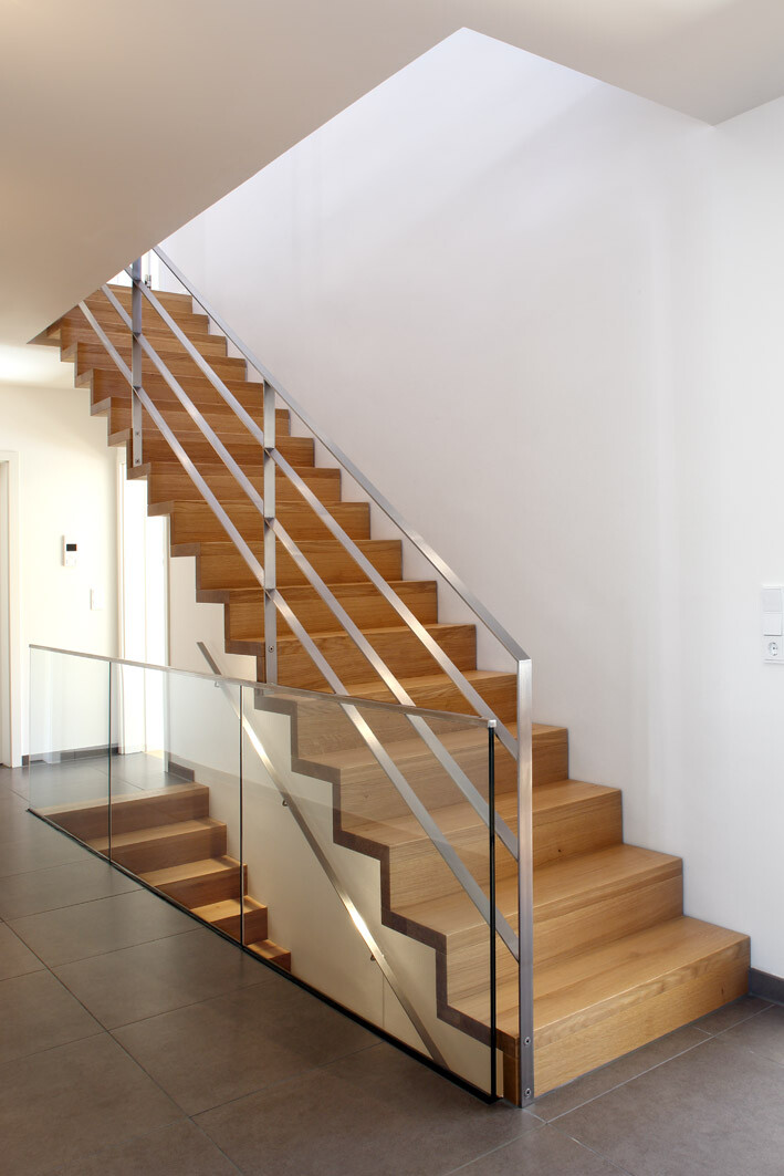 Moderne Holztreppe mit Glas- und Metallgeländer im hellen Innenraum.