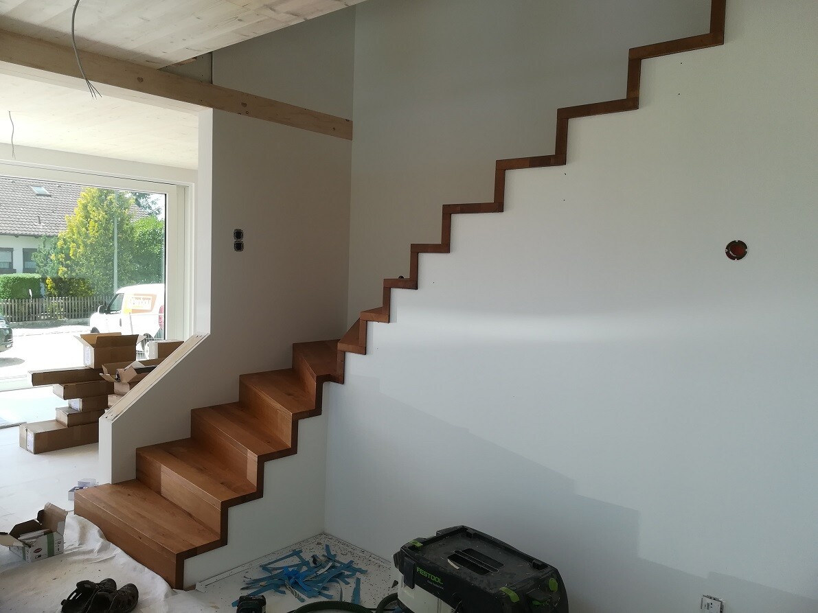 Helle Neubauwohnung mit Holztreppe in Zickzack-Form an der weißen Wand, Bauwerkzeuge im Raum.