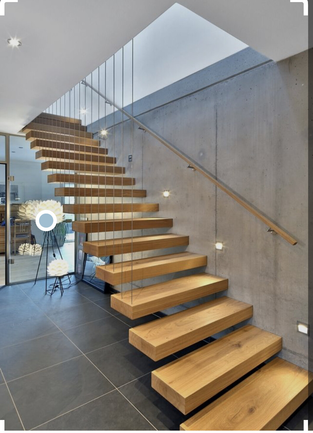 Moderne Holztreppe mit Glasgeländer in Loftwohnraum, Betonwand und Beleuchtung.