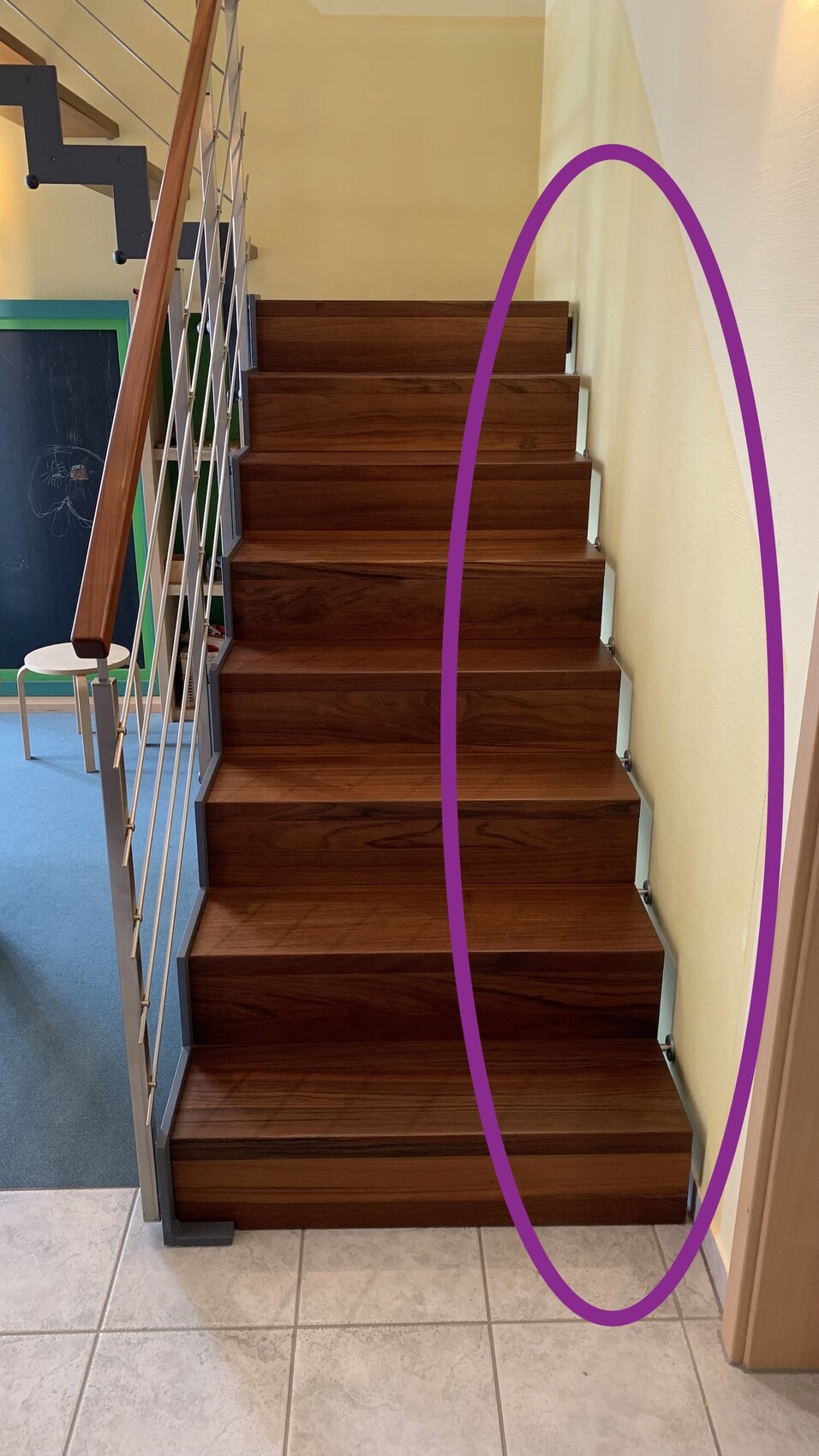Holztreppe mit Metallgeländer links, gelbe Wand rechts, violette Markierung am Rand.