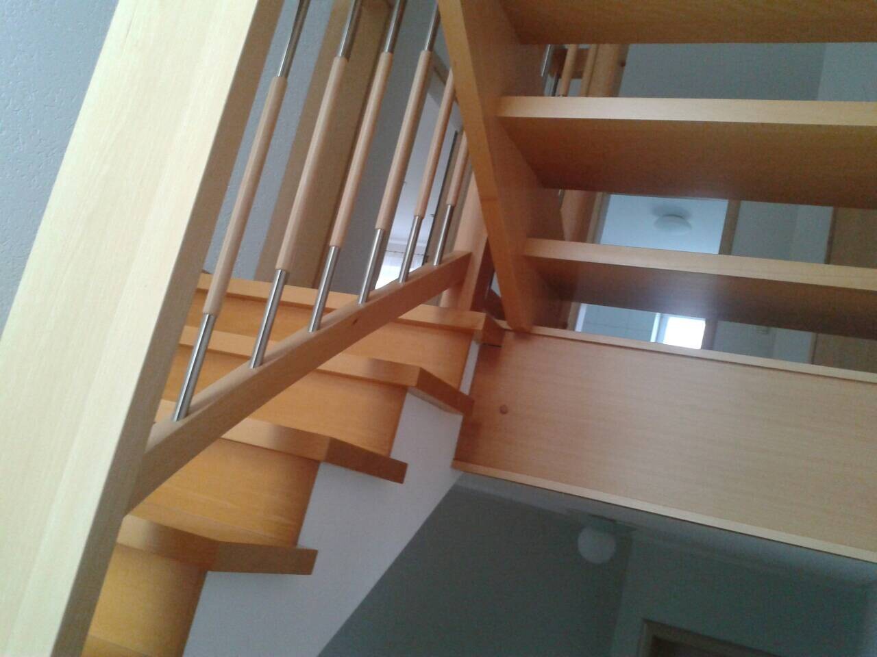 Holztreppe mit Geländer aus Metallstäben, Blick von unten im Innenraum.
