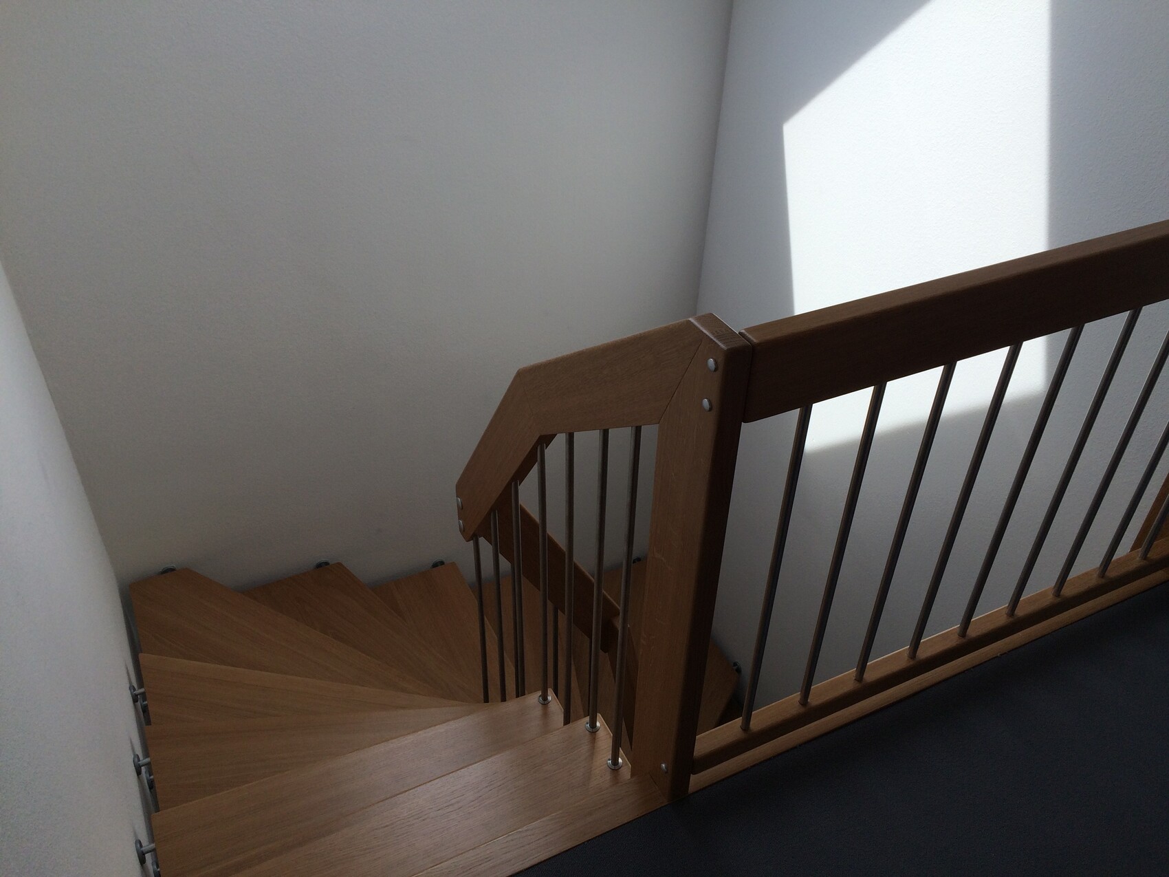 Holztreppe mit Holzgeländer und Metallstäben, Innenraum; Licht wirft Dreiecks-Schatten an Wand