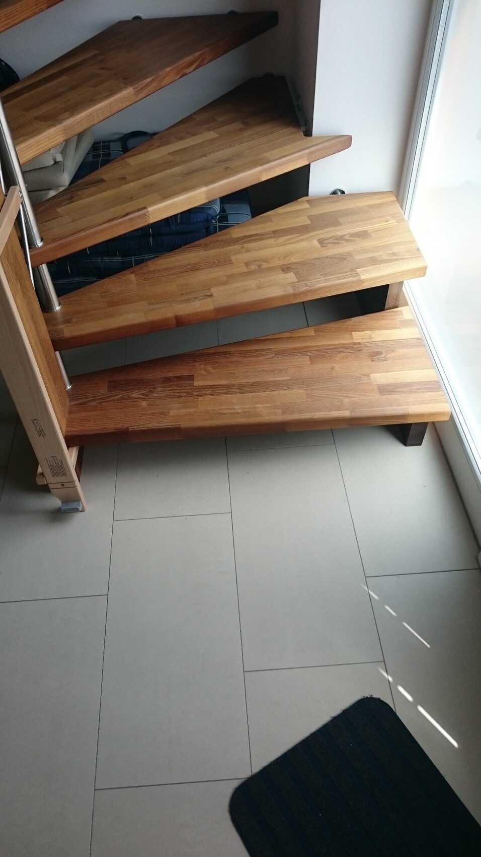 Moderne freischwebende Holztreppe mit Metallpfosten neben großem Glasfenster in Wohnung