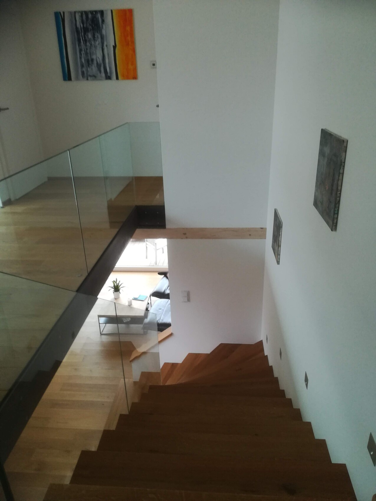 Moderne Holztreppe mit Glasgeländer, Blick ins Wohnzimmer im unteren Bereich.