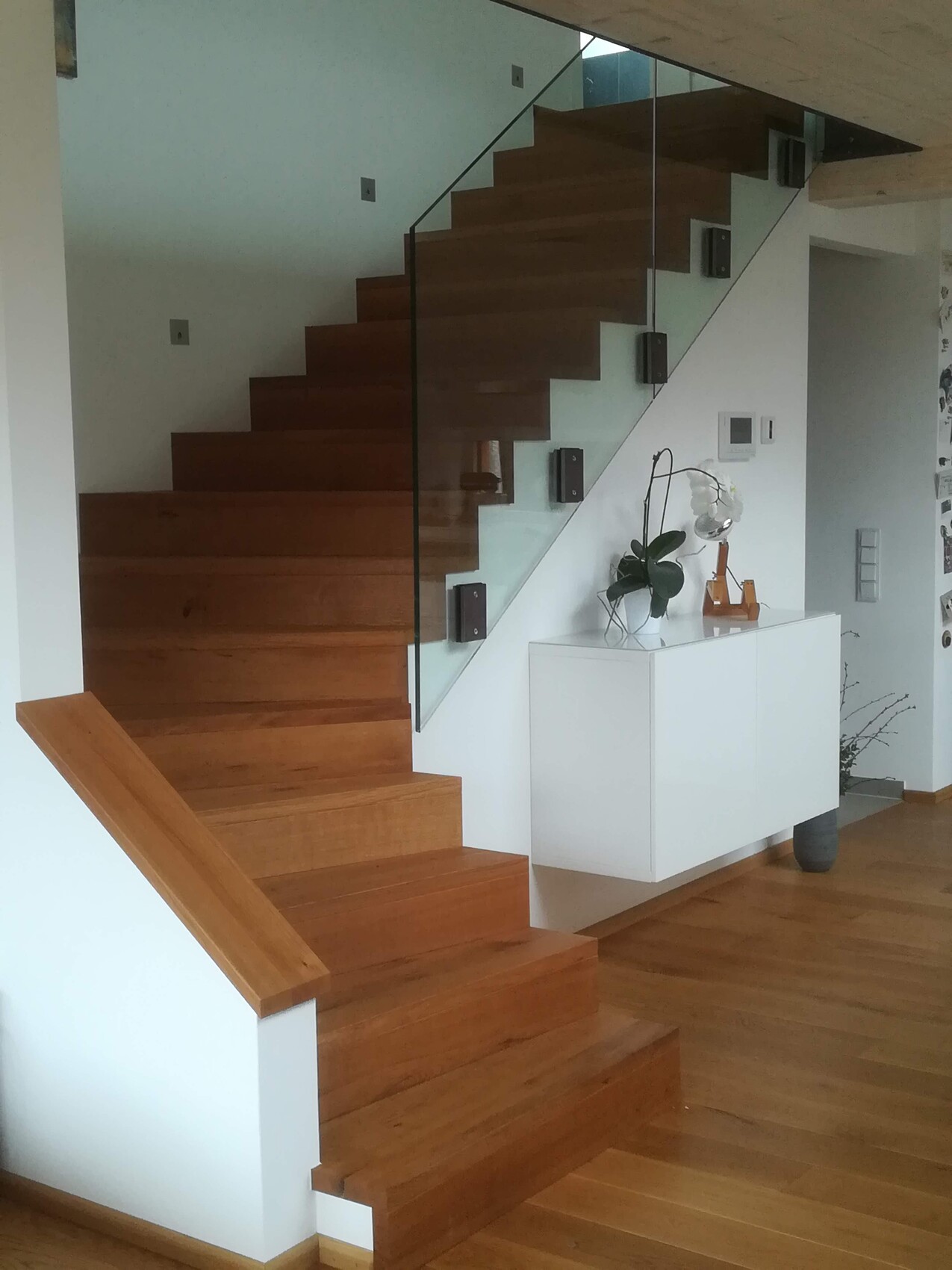 Moderne Holztreppe mit Glasgeländer, weißes Sideboard mit Pflanze und Lampe