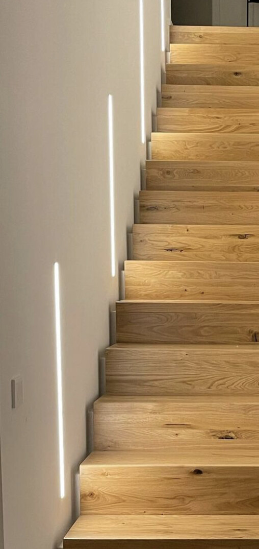 Moderne Holztreppe mit LED-Lichtstreifen an weißer Wand, führt nach oben.