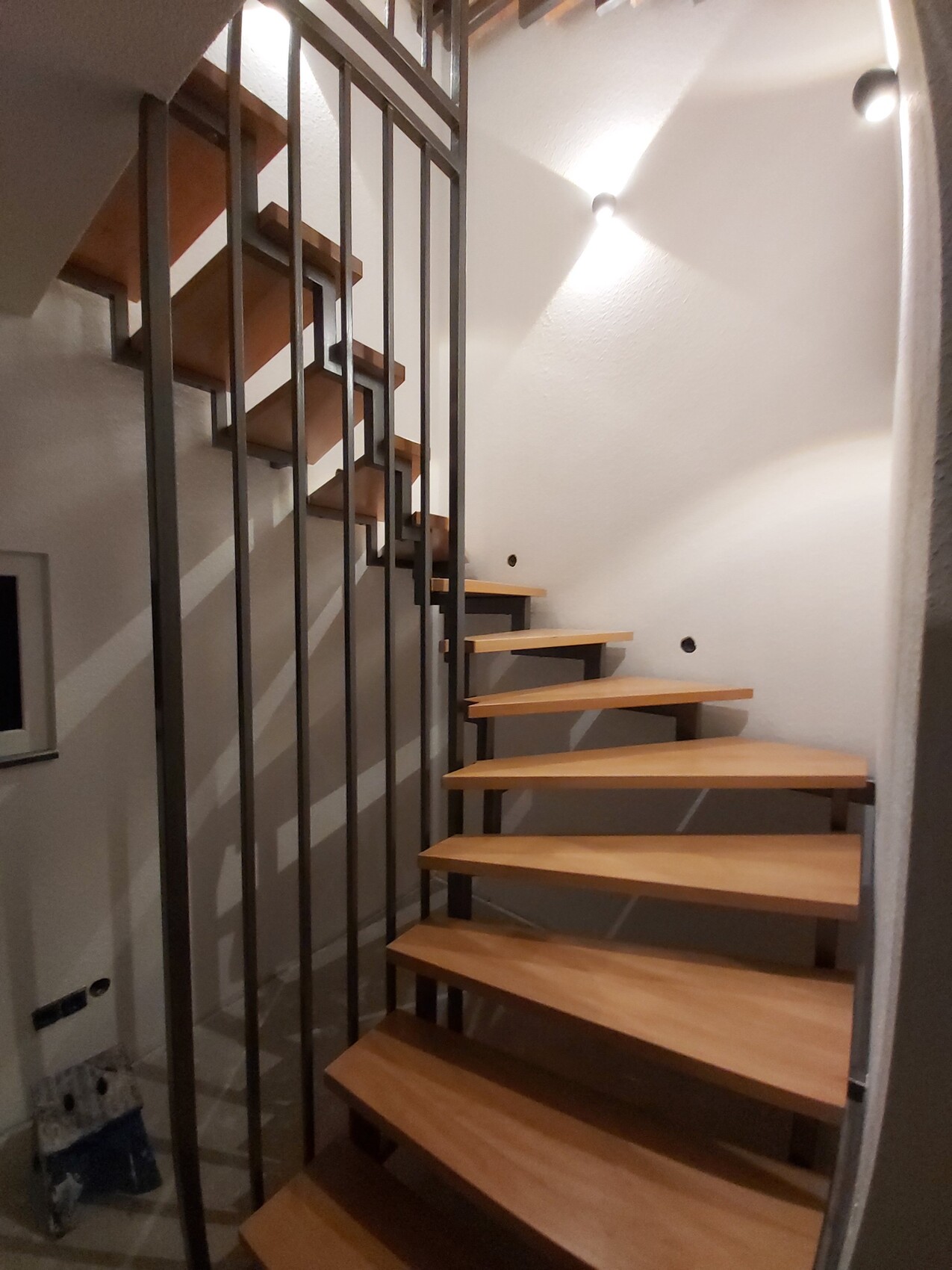 Spiralförmige Holztreppe mit schwarzem Metallgeländer im hellen Innenraum, Blick von unten.