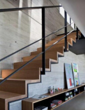 Moderne Holztreppe mit Stahlgeländer in hellem Wohnbereich und Bücherregal