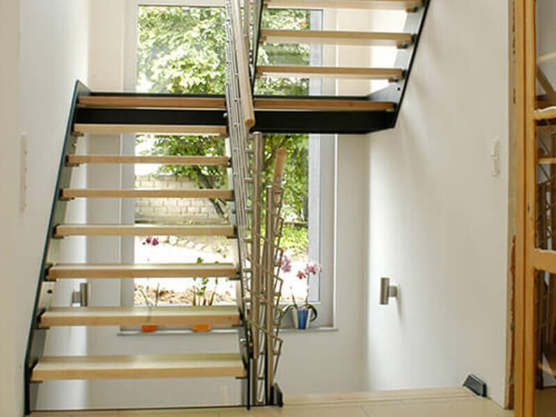 Moderne Treppe mit offenen Holzstufen und Metallrahmen, Fensterblick nach draußen.