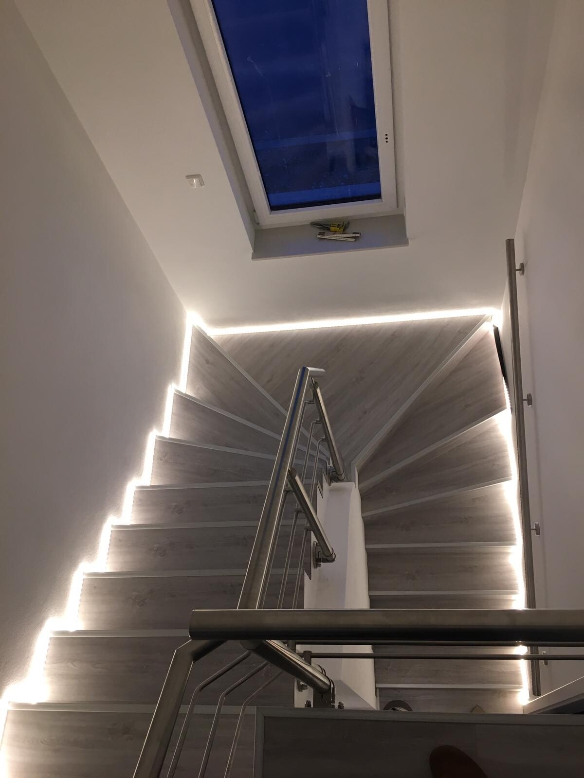 Moderne Treppe mit LED-Stufenbeleuchtung, Edelstahl-Handlauf und Dachfenster.
