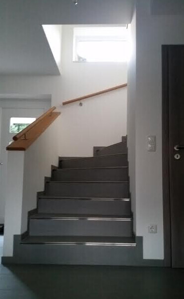 Innenansicht: dunkle Treppe mit Holzhandlauf, Fenster oben, Tür rechts