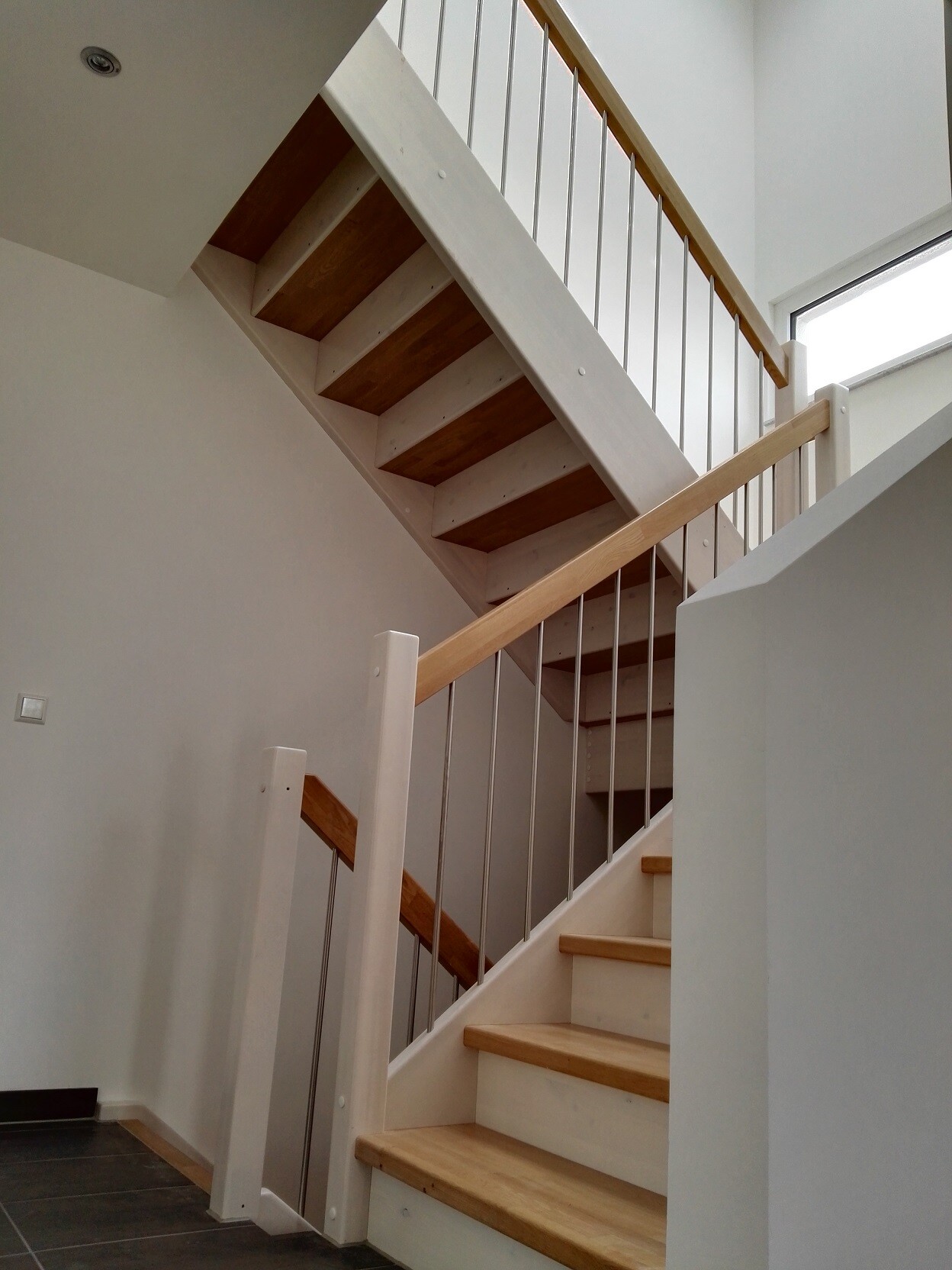 Moderne Innentreppe mit Holzstufen, weißen Geländern und Metallstäben im hellen Innenraum.