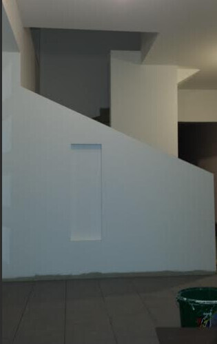 Innenansicht eines Treppenbereichs mit weisser Wand, grauer Boden und Eimer