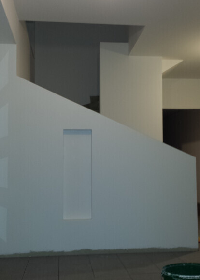 Moderne weiße Innenwand mit diagonaler Schräge, vertikaler Nische und dunklem Hintergrund.
