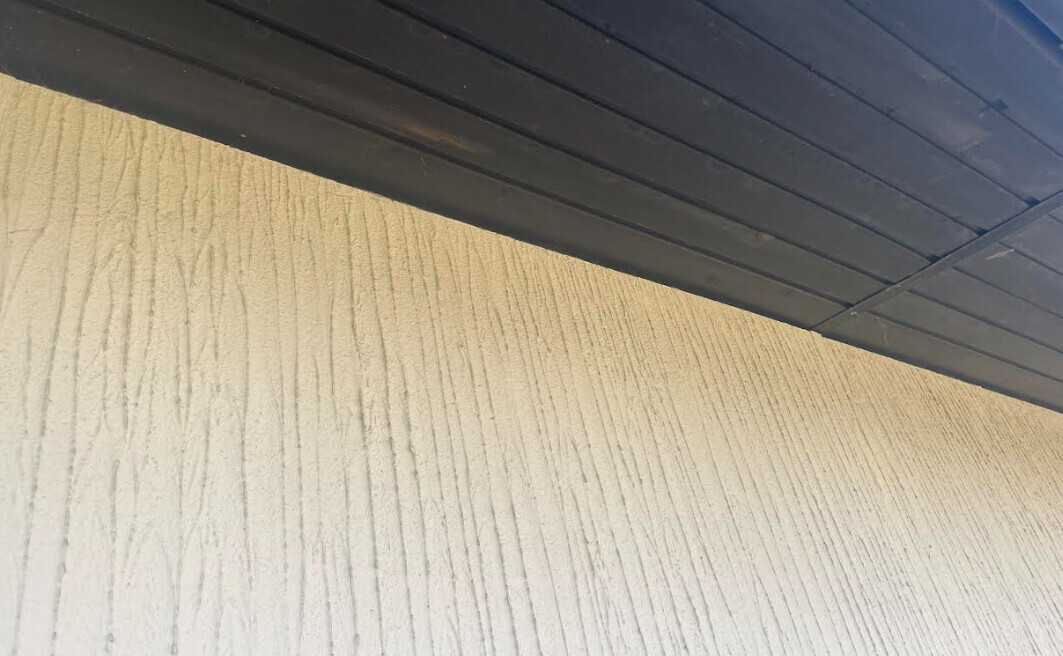 Nahaufnahme einer beige Wand mit vertikalen Rillen unter einer dunklen Deckenverkleidung.