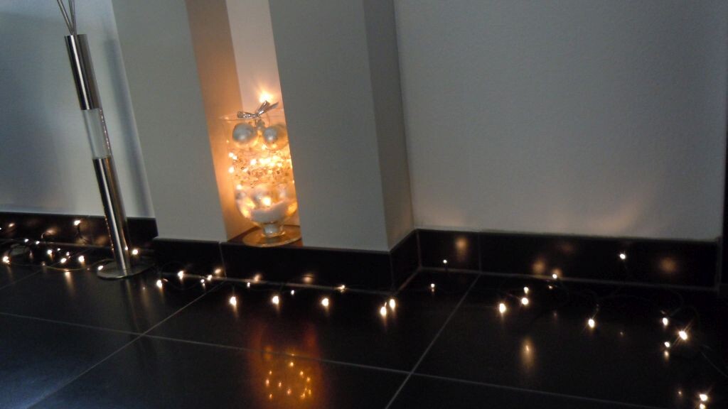 Moderne Innenbeleuchtung mit LED-Lichterkette entlang dunkler Bodenfliesen und Dekorlampe.