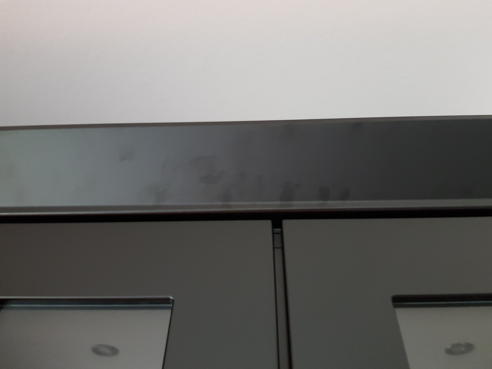 Graue Schranktüren mit horizontaler Glasleiste oben, dunkler Korpus und Spuren von Fingerabdrücken