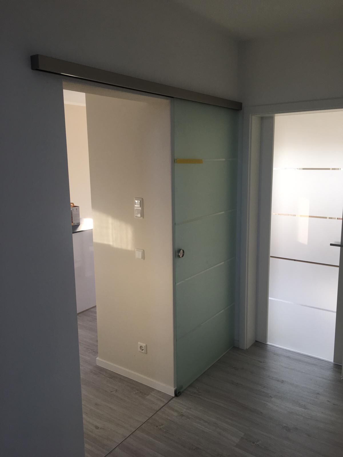 Moderner Flur mit Glas-Schiebetür, heller Innenraum und grauen Laminatboden.