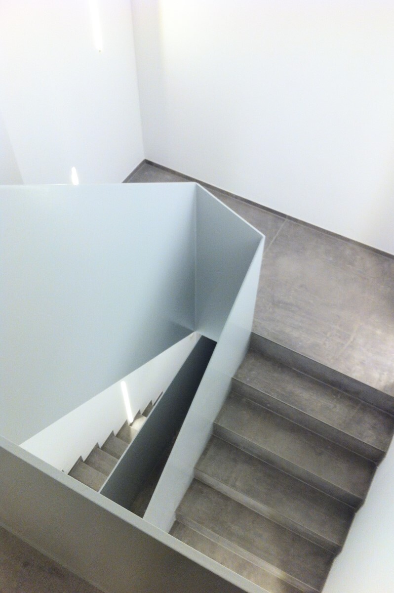 Blick von oben auf eine moderne graue Treppe mit seitlicher Trennwand im Innenraum.