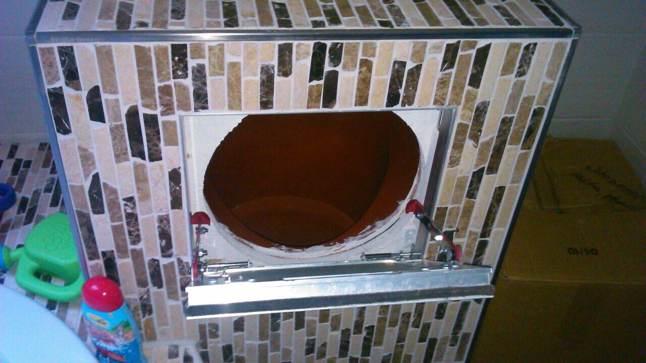 Kachelofen mit rundem Brennraum und mosaikverkleideten Fliesen in einer Bauumgebung