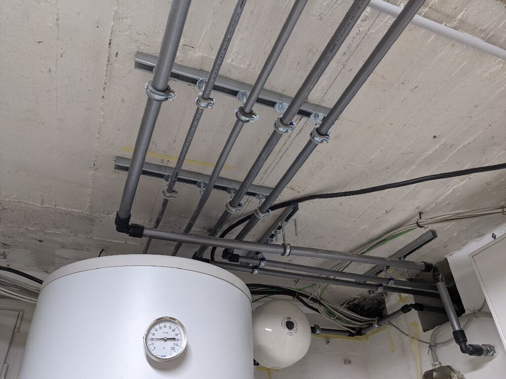 Großer Warmwasserspeicher mit Druckmesser, Rohrleitungen an Beton-Decke