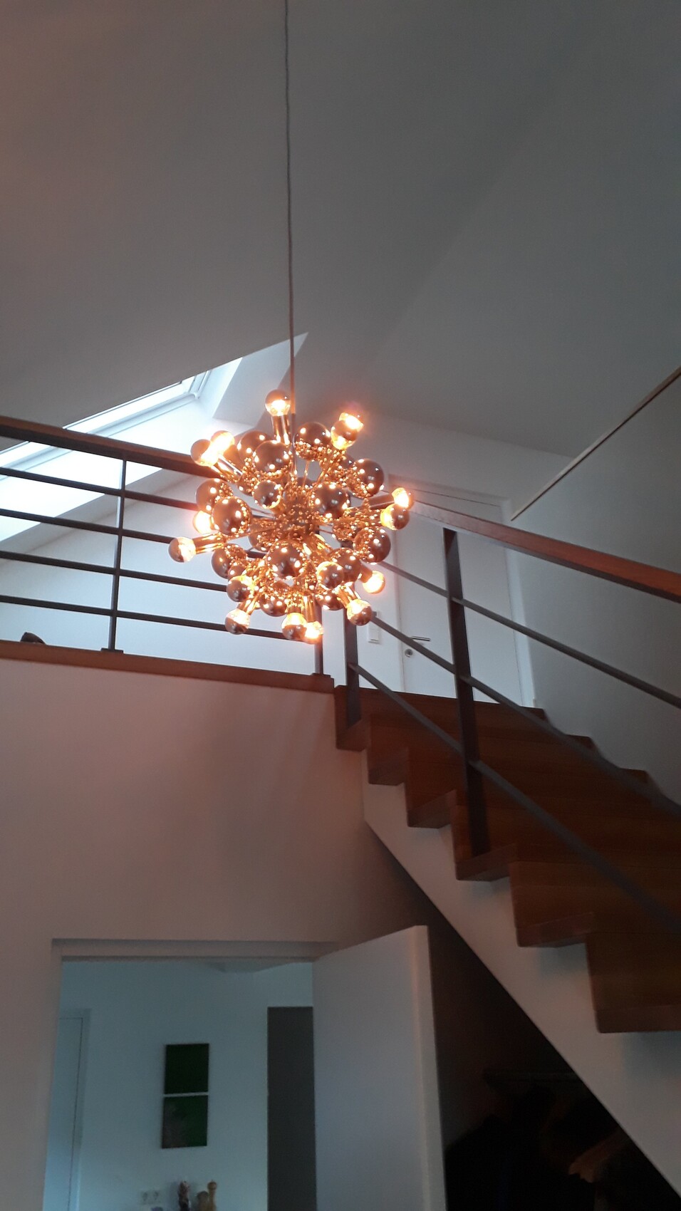 Moderne Kugellampe mit vielen Glühbirnen hängt von der Decke über offener Treppe.