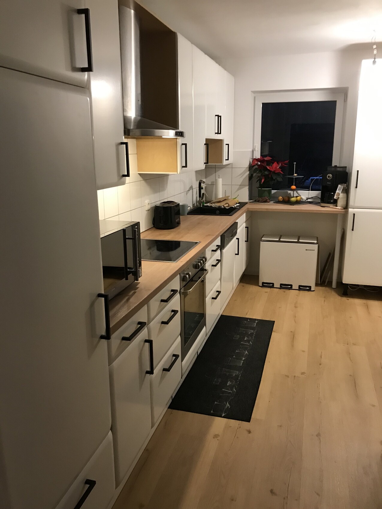 Moderne Küche: weiße Schränke, Holz-Arbeitsplatte, Ofen, Kochfeld, Fenster mit Pflanze.