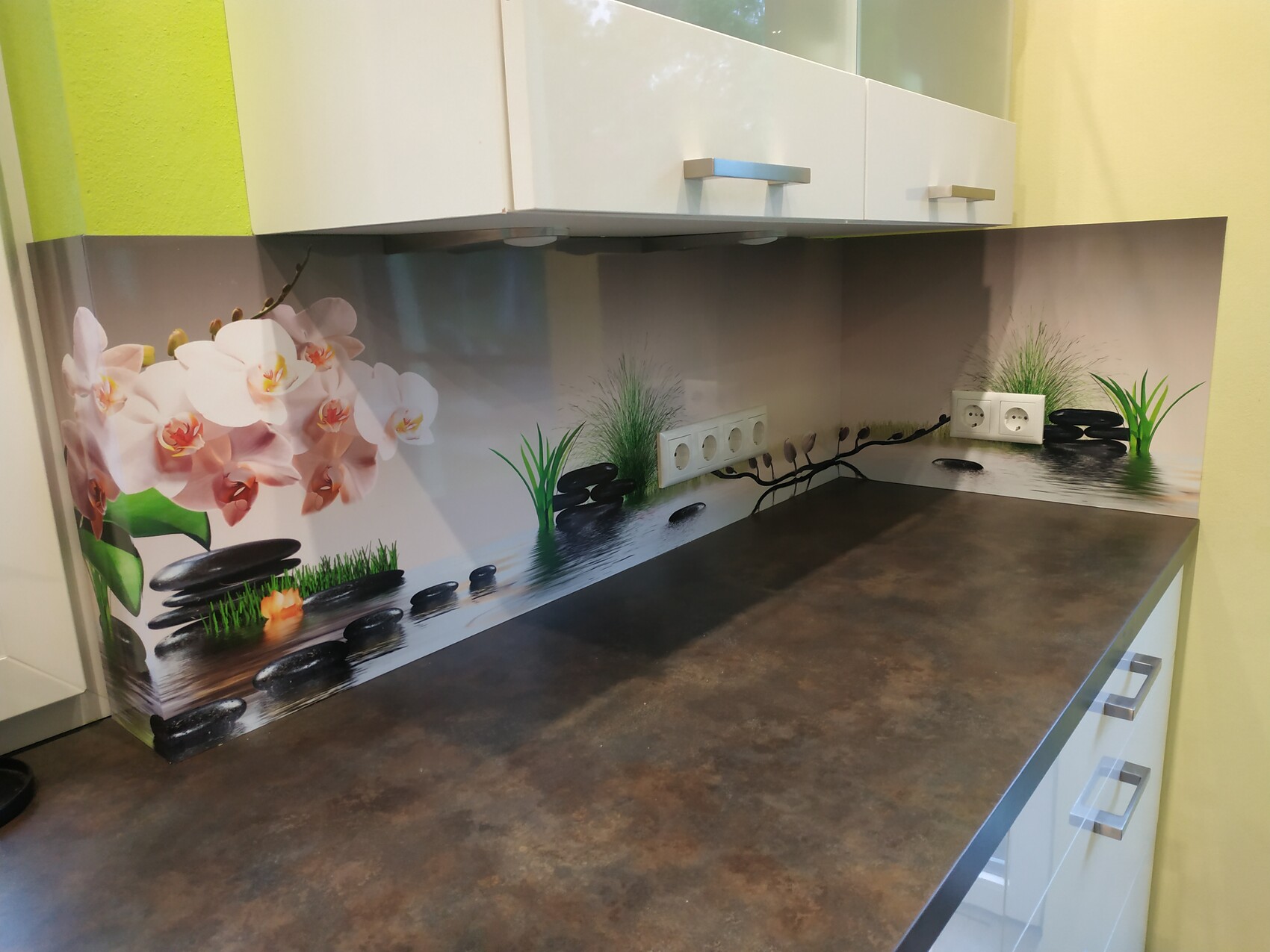 Küche mit brauner Arbeitsplatte und Rückwand mit Orchideen, Steinen und Gras am Wasser; Steckdosen.