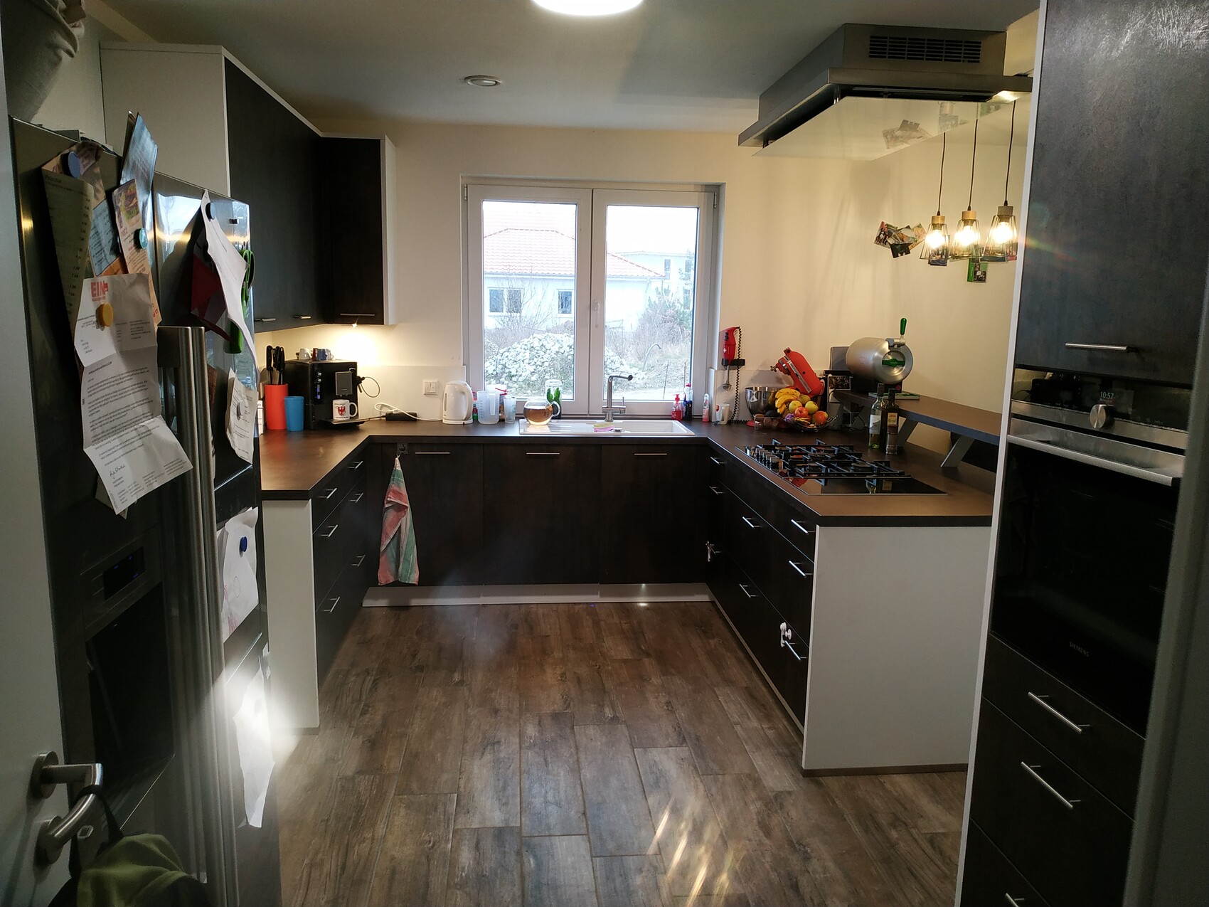 Moderne Küche mit dunklen Schränken, Holzboden, Fenster über der Spüle und Backofen rechts.