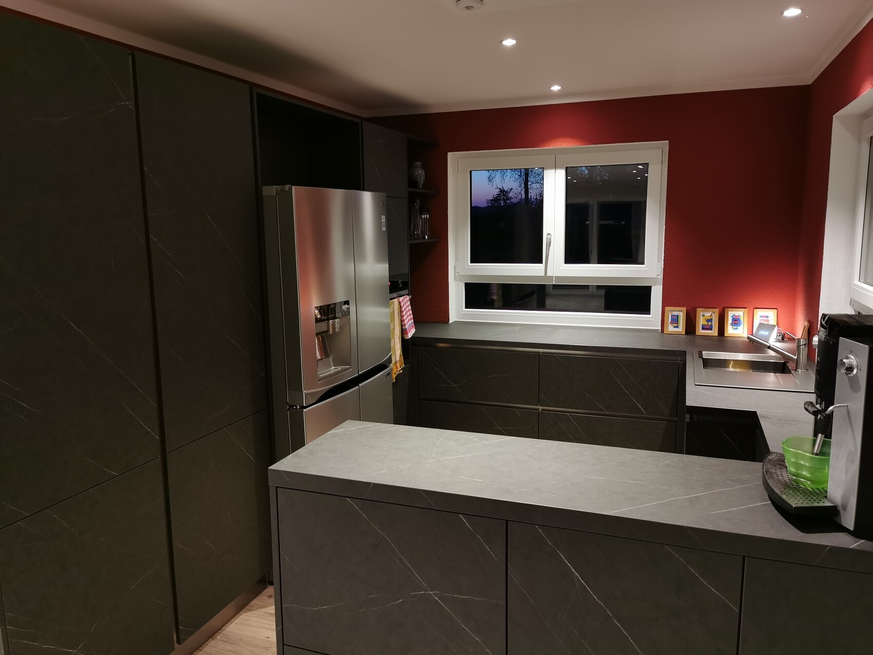 Moderne Küche mit grauen Arbeitsplatten, dunklen Schränken, Edelstahlkühlschrank und Fenster.