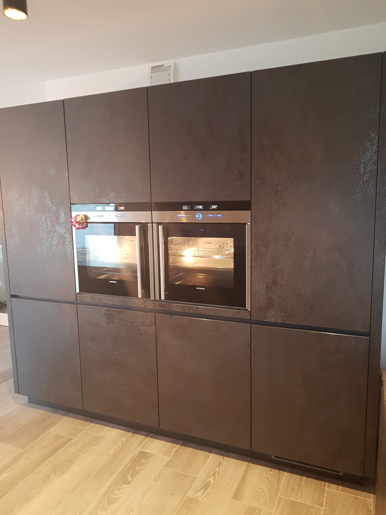 Moderne Küche mit dunkelmatten Fronten, zwei integrierte Backöfen, Holzfußboden.