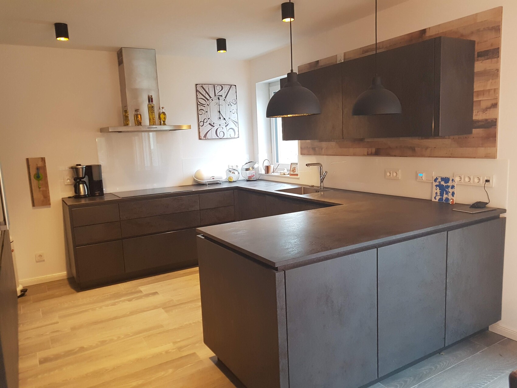 Moderne Küche mit dunklen Schränken, Kücheninsel, Holzwand, Pendelleuchten und Spüle
