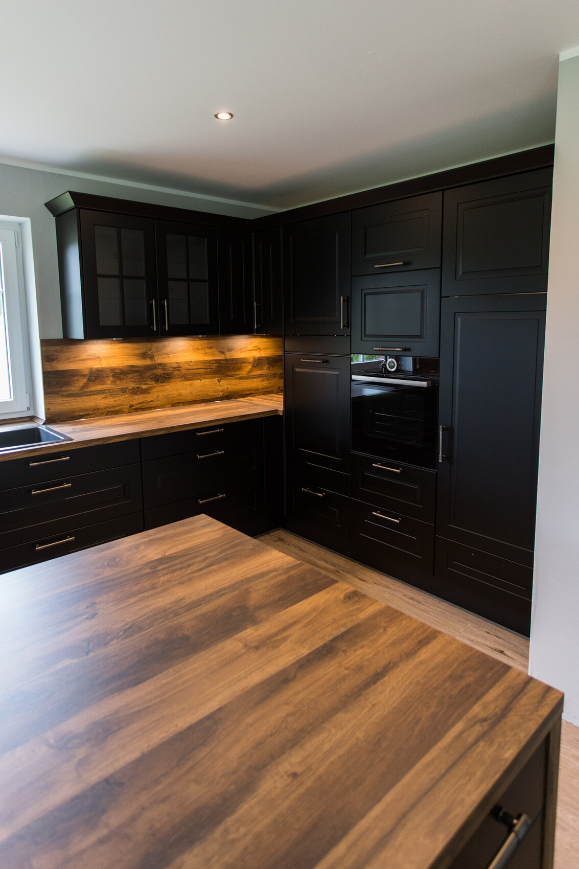 Moderne schwarze Küche mit Holz-Arbeitsplatte, Eckschränken und Backofen.