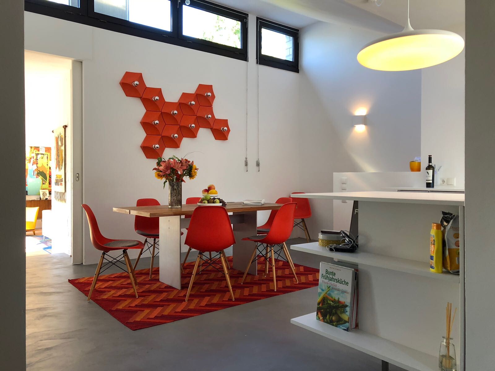 Essbereich mit rotem Teppich, Holztisch und roten Stühlen, Vase Blumen, rote Hexagon-Wanddeko.