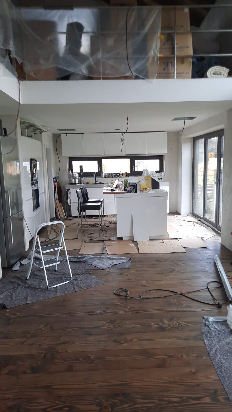 Offene Küche während Renovierung: Kartonabdeckungen, Leiter, Kabel, Werkzeuge, Holzboden.