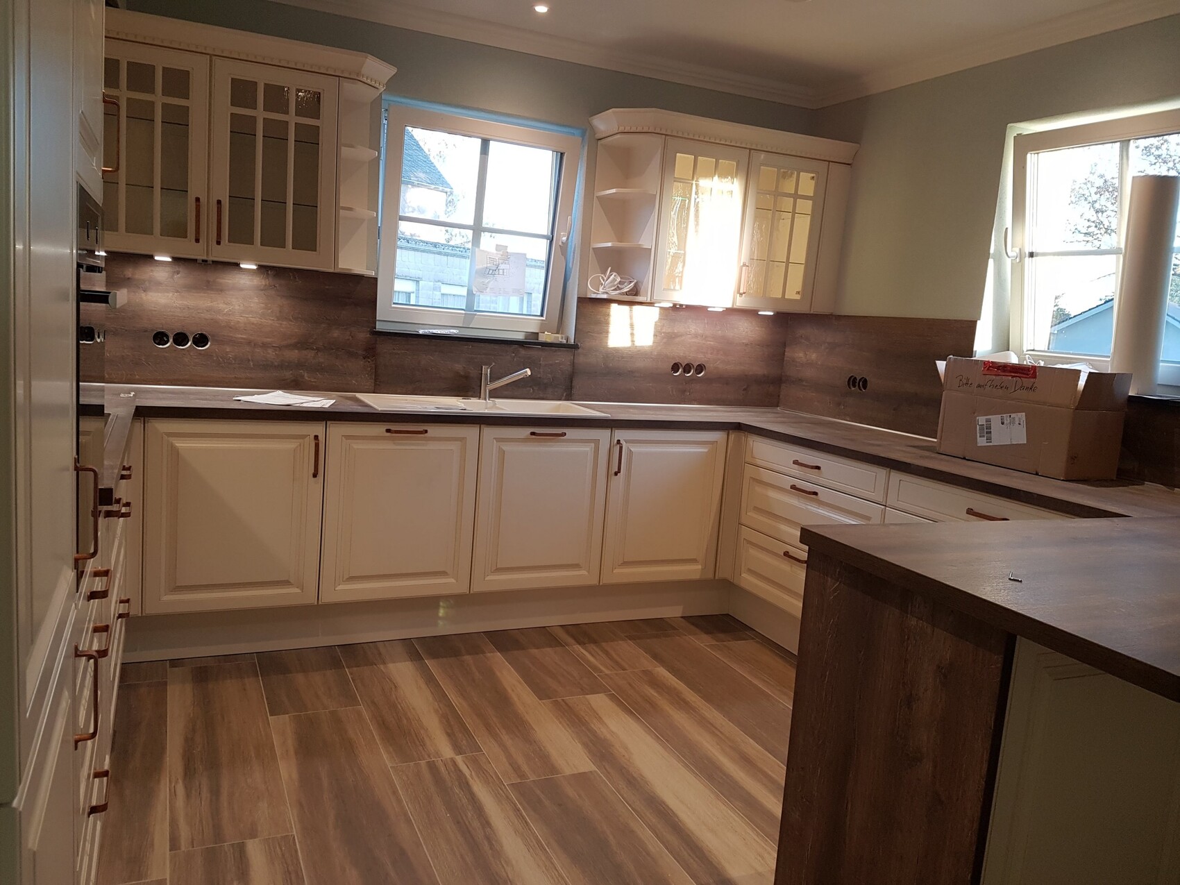 Moderne Küche mit weißen Schränken, Holz-Arbeitsplatten, Spüle und Kartonbox auf der Theke.