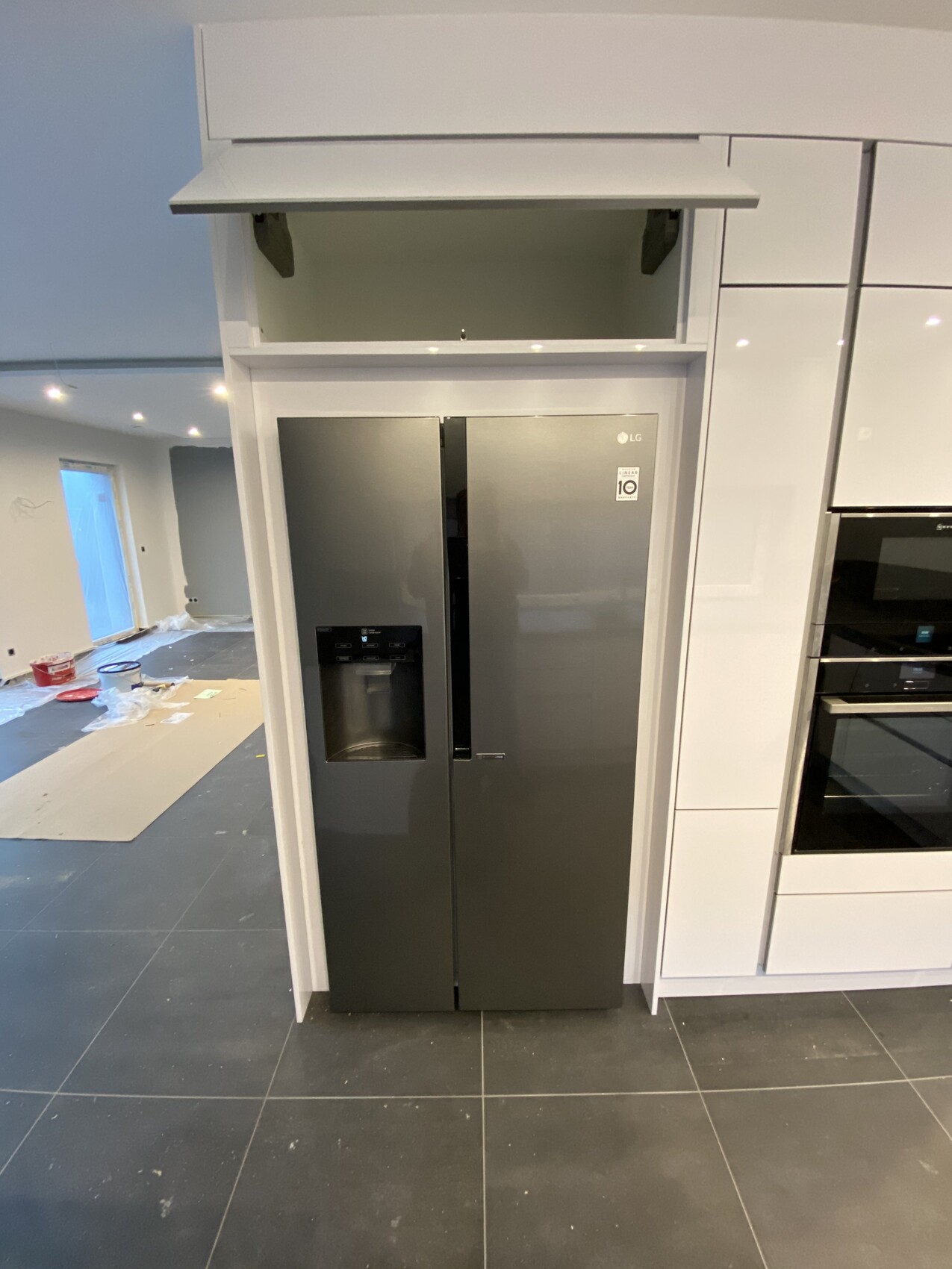Grau glänzender Side-by-Side-Kühlschrank mit Wasserspender in einer weißen Küchenzeile unfertig