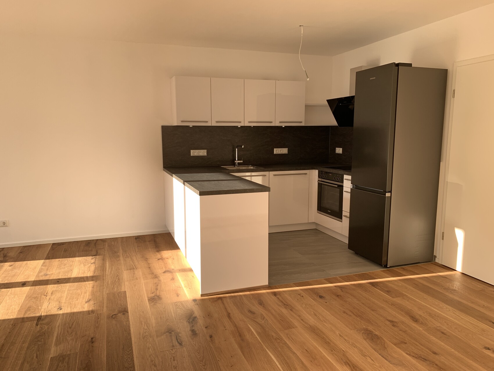 Moderne Küche mit Insel, weißen Oberschränken, dunkler Arbeitsplatte, Ofen, Kühlschrank, Holzfußboden.