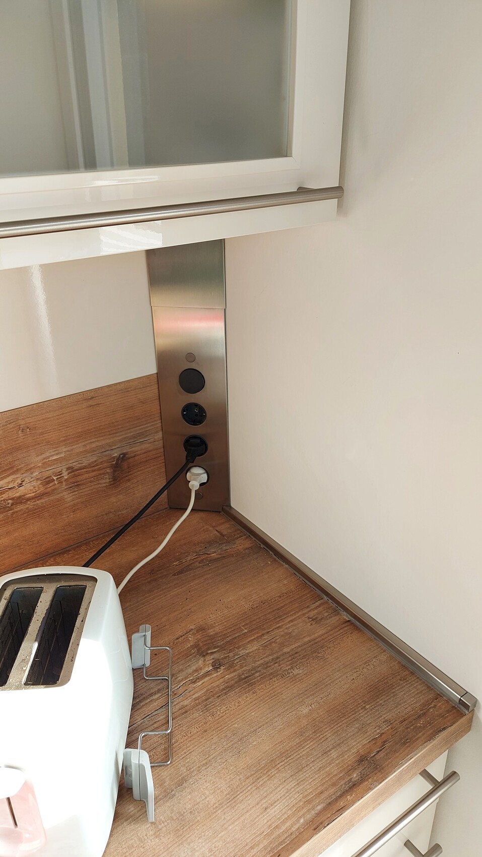 Helles Küchenarrangement: Toaster auf holzfarbener Arbeitsplatte neben Edelstahl-Steckdosenleiste