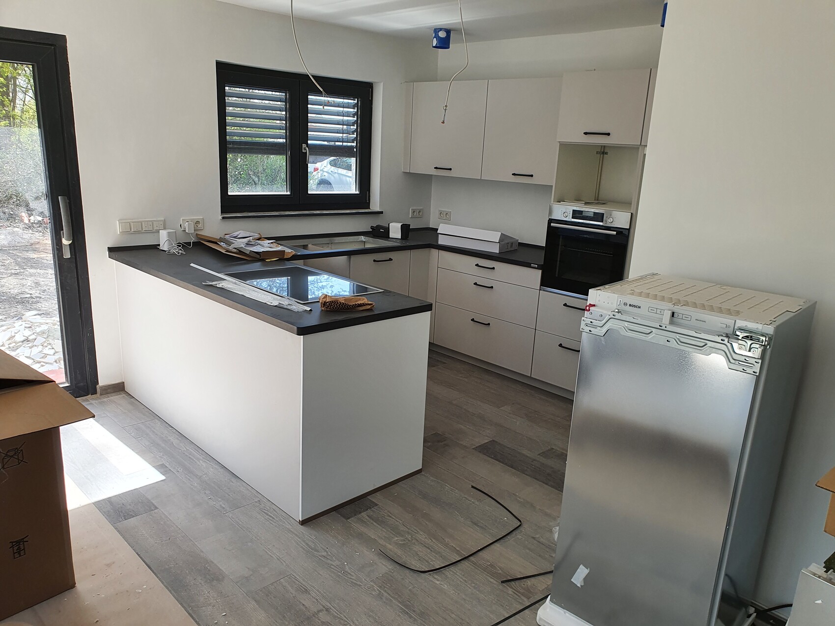 Moderne Küche im Bau mit Insel, weißen Schränken, schwarzen Arbeitsplatten und eingebautem Ofen.