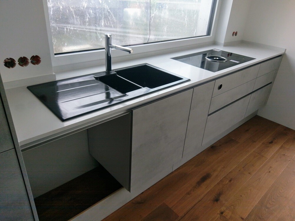 Moderne Küchenzeile mit Spüle, dunkler Arbeitsplatte und Induktionskochfeld vor Fenster