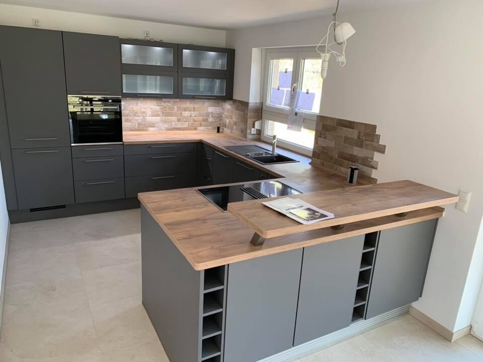 Moderne Küche mit grauen Fronten, Holz Arbeitsplatten, Spüle am Fenster, Insel mit Kochfeld.