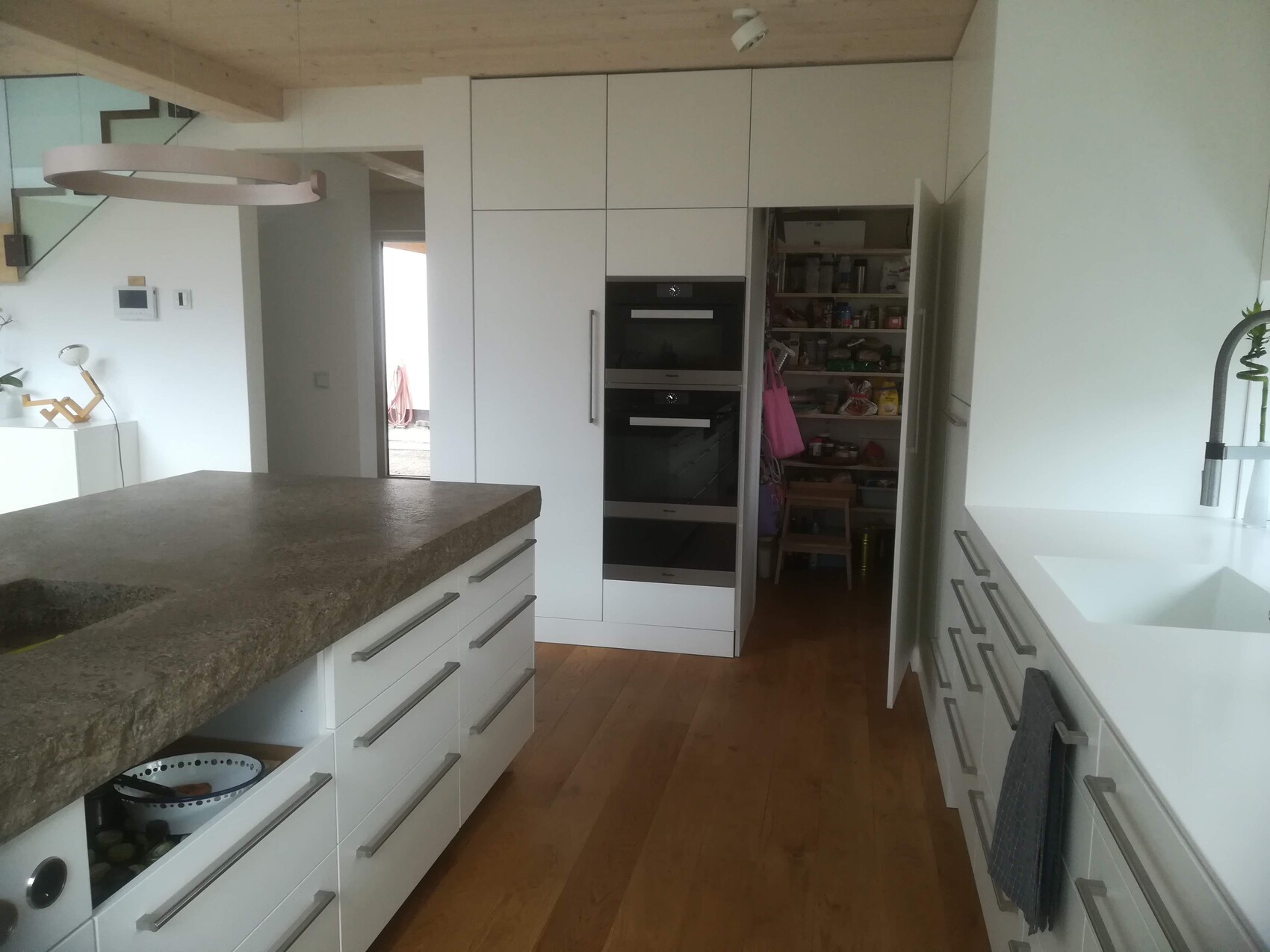 Moderne weiße Küche mit Insel aus Stein, Backöfen und offenem Vorratsschrank.