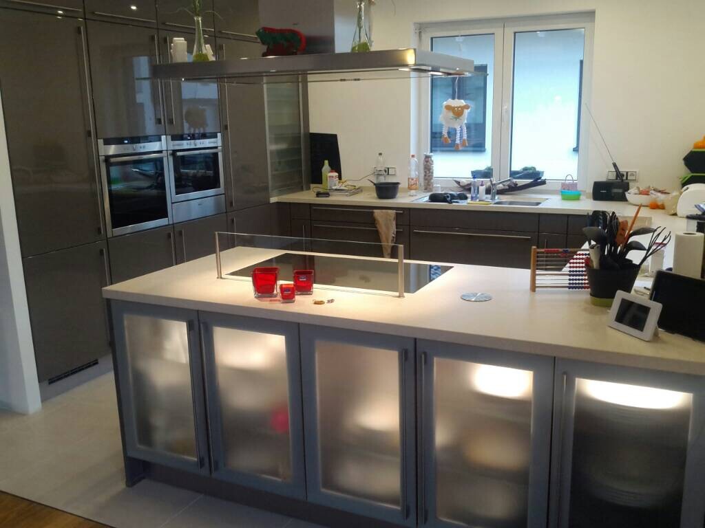 Moderne Küche mit Insel, Edelstahlgeräten und roten Gläsern auf der Arbeitsfläche.