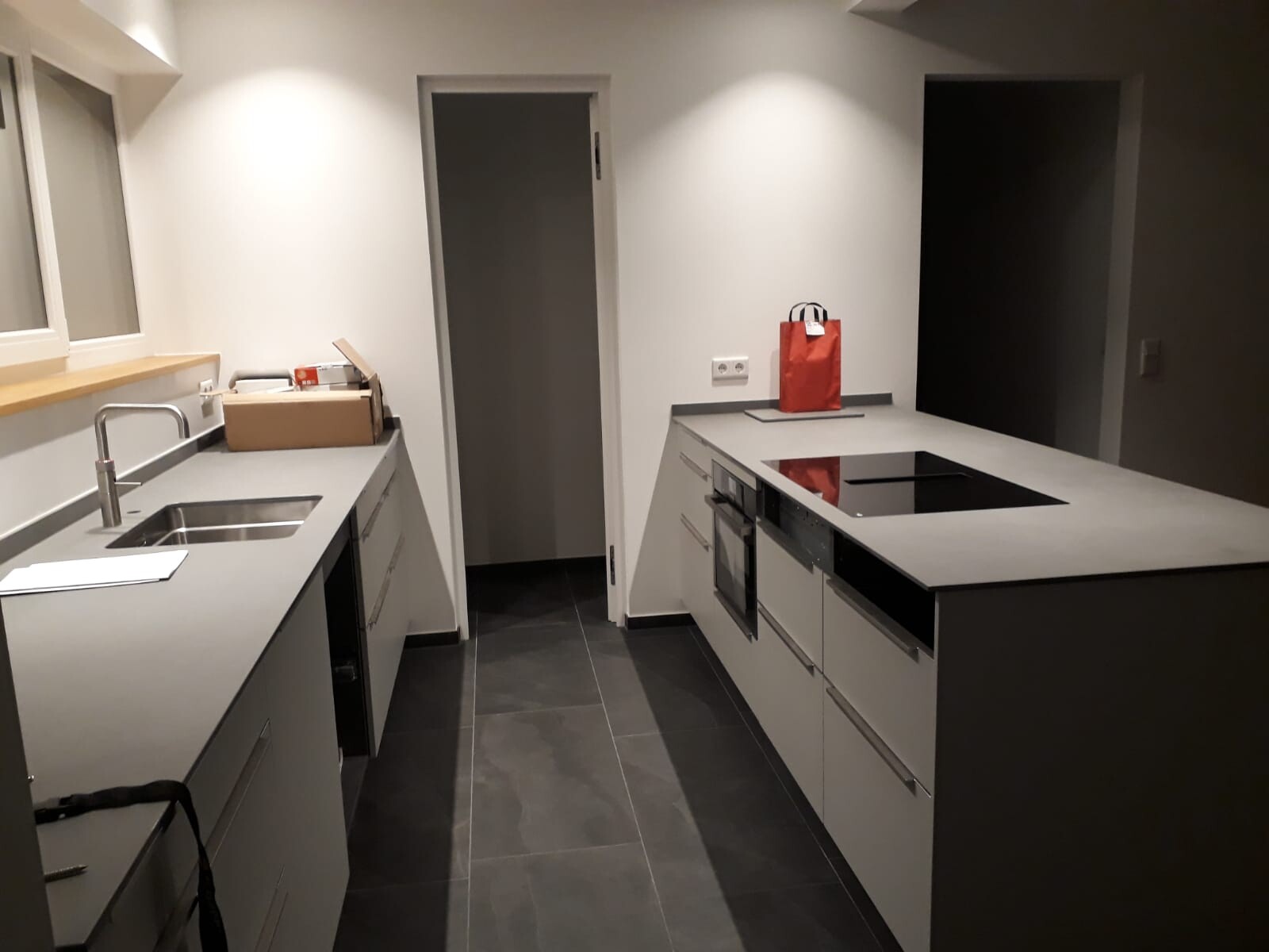 Moderne Küche mit grauen Arbeitsplatten, Spüle, Induktionskochfeld und Ofen; rote Tüte.