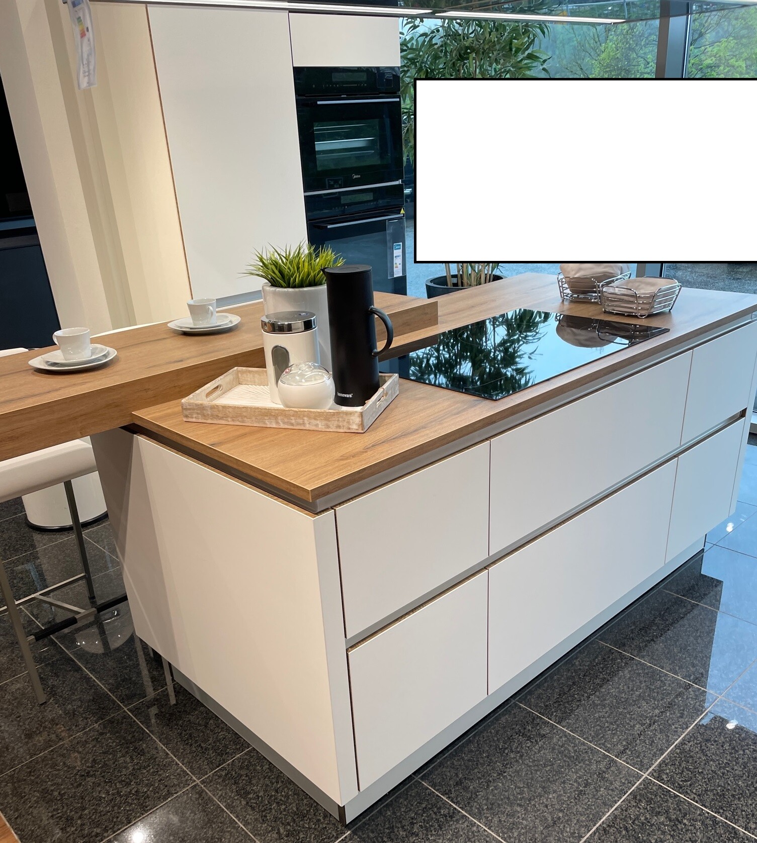 Moderne Kücheninsel mit Holzoberfläche, Induktionskochfeld, Backofen, Kaffee-Setup und Pflanze.