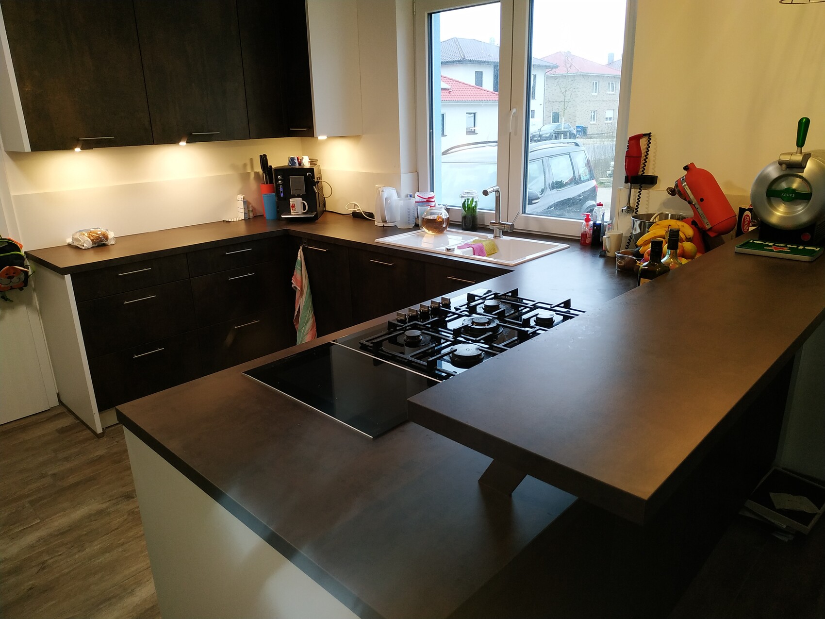 Moderne Kochküche mit dunklen Schränken, Kochinsel, Gasherd, Spüle am Fenster und Küchengeräte.