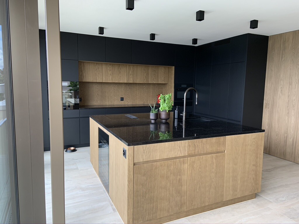 Moderne Küche mit Holzinsel, schwarzen Schränken, dunkler Arbeitsplatte, Spüle und Pflanzen