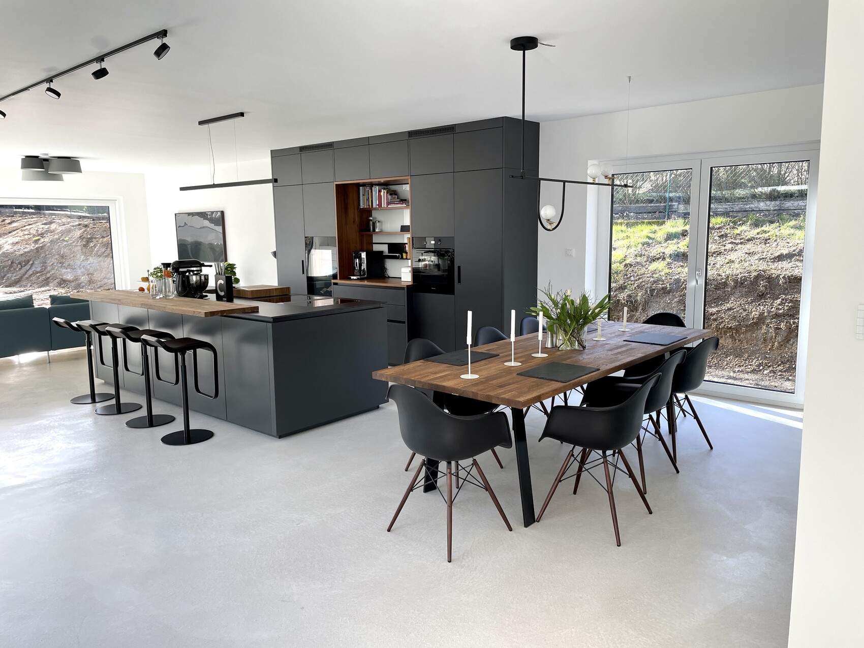 Moderne offene Küche mit grauer Insel, Holz Esstisch, schwarze Stühle, große Fenster zum Garten